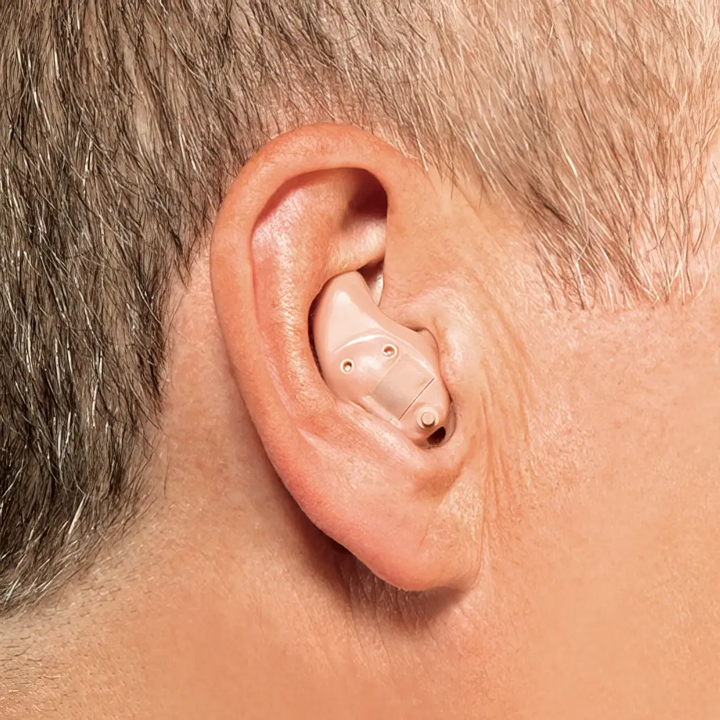 A close-up of a person's ear displaying a beige hearing aid fitted inside the ear canal.