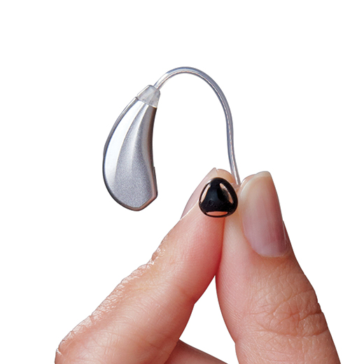 A person holds a small black hearing aid component with a thin wire, designed for ear use.